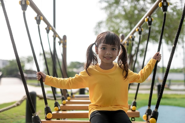 Linda niña pequeña divirtiéndose en el patio de recreo escalando y deslizándose hacia abajo