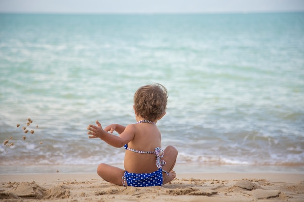 Linda niña pequeña jugando en la arena de la playa del océano vista posterior