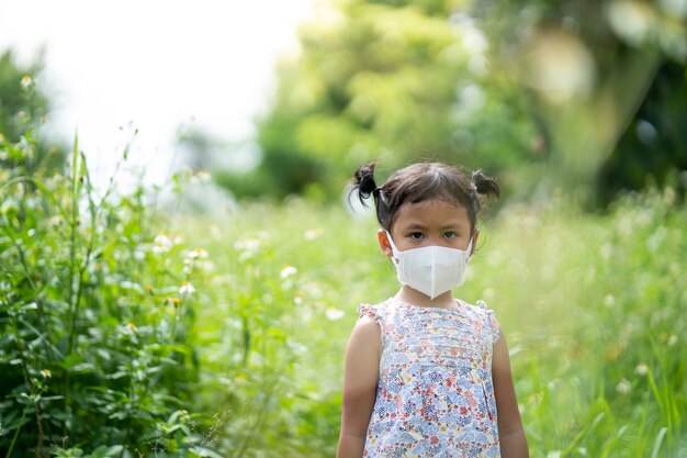 Linda niña pequeña con mascarilla protectora de pie en el campo