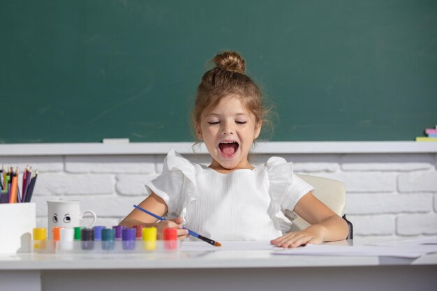 Linda niña pequeña pintando con pinturas de color y pincel pintando la lección de la escuela dibujando arte