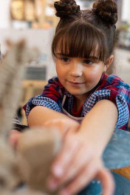 Linda niña preescolar de ojos oscuros se siente involucrada n esculpir arcilla