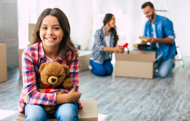 Una linda niña que sostiene con fuerza a su adorable osito de peluche tiene una amplia sonrisa sincera en su rostro por estar extremadamente feliz por un nuevo hogar.