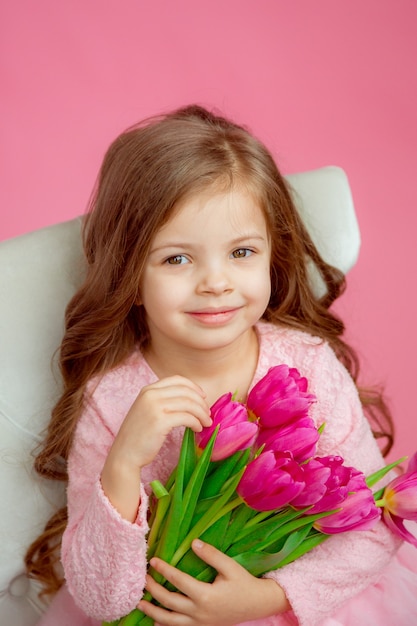 Linda niña con un ramo de tulipanes en sus manos sobre un fondo rosa