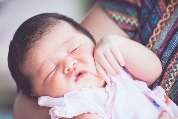 Linda niña recién nacida asiática durmiendo en el brazo de la madre