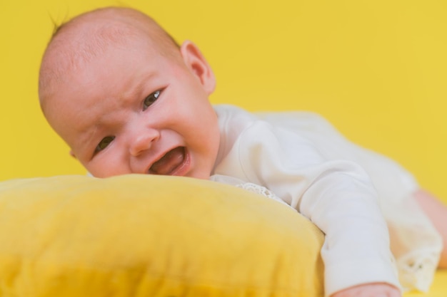 Linda niña recién nacida grita y llora en un primer plano de almohada amarilla