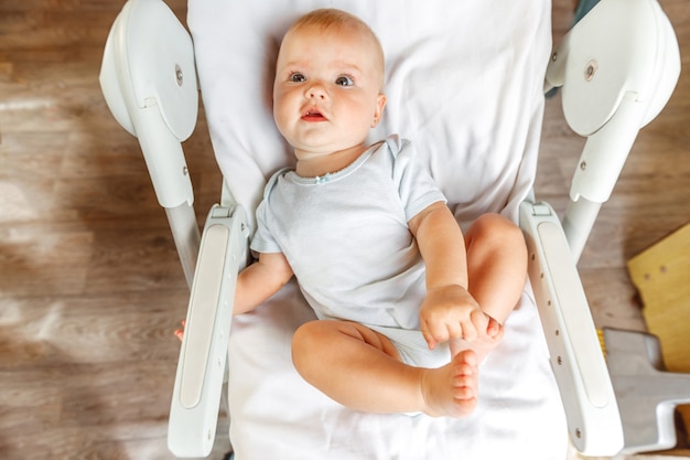 Linda niña recién nacida con rostro sonriente mirando a cámara sobre fondo blanco. Bebé descansando jugando acostado en la silla de alimentación en casa. Concepto de niño feliz de maternidad.