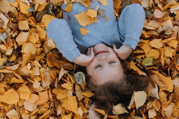 linda niña recostada sobre hojas amarillas en el parque en el otoño banner de tarjeta de otoño saludable