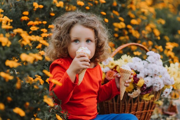 linda niña rizada comiendo helado en el parque tiempo de otoño tarjeta de otoño banner de flores