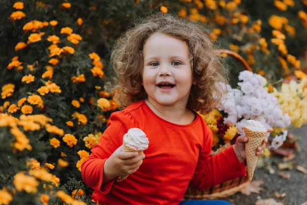 linda niña rizada comiendo helado en el parque tiempo de otoño tarjeta de otoño banner de flores