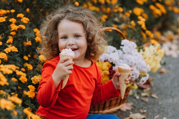 linda niña rizada comiendo helado en el parque tiempo de otoño tarjeta de otoño banner de flores