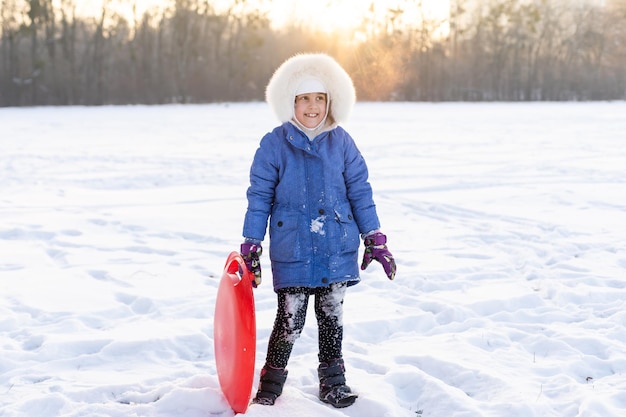 una linda niña con ropa de invierno juega en el parque con trineos. las vacaciones de invierno.