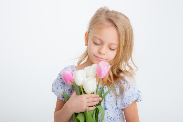 Linda niña rubia en la celebración de un ramo de flores de primavera sobre un fondo blanco.