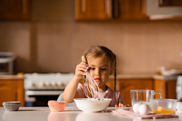 Foto linda niña rubia cocinando masa en la cocina en casa