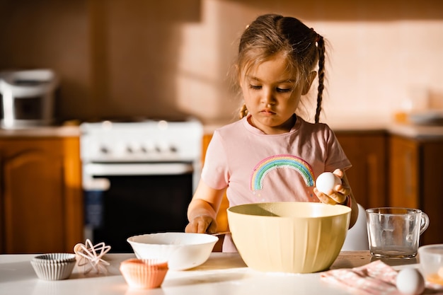 Linda niña rubia cocinando masa en la cocina en casa