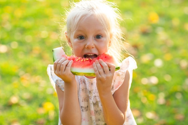 Linda niña rubia comiendo sandía en el césped en el parque