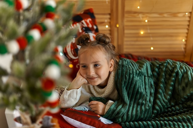 Linda niña rubia durmiendo bajo el árbol de Navidad