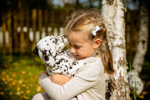 Linda niña rubia jugando con su cachorro dálmata al aire libre en la soleada y cálida guardería de mascotas de otoño