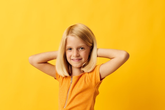 Linda niña rubia pelo lacio posando sonrisa diversión fondo amarillo inalterado