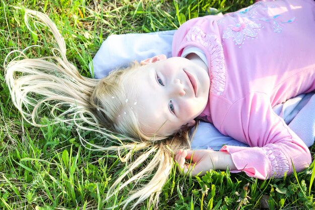 Linda niña rubia con pétalos blancos de cerezo de pájaro en su cabello acostado en el prado verde en el parque de primavera