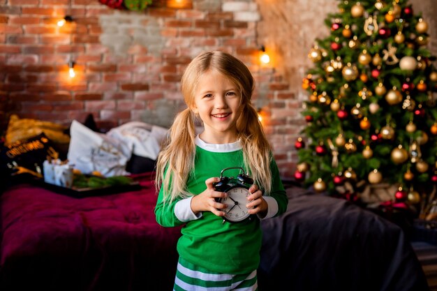 Linda niña rubia en pijama cerca del árbol de Navidad