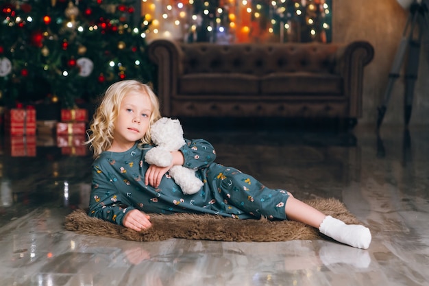 Linda niña rubia posando en el árbol de Navidad