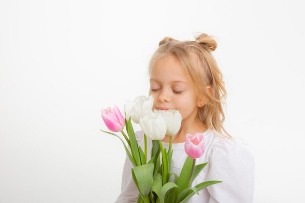 Linda niña rubia con un vestido que sostiene un ramo de flores de primavera en un fondo blanco