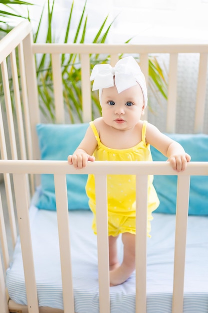 Linda niña sana está de pie en una cuna por la mañana mirando a la cámara el concepto de productos para bebés el concepto de sueño del bebé