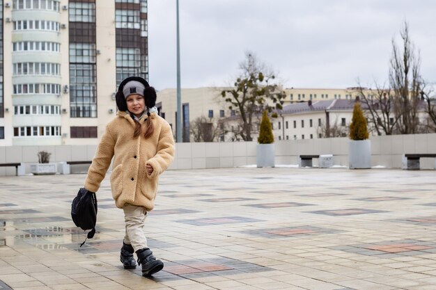 una linda niña de seis años camina por la plaza de la ciudad con una mochila