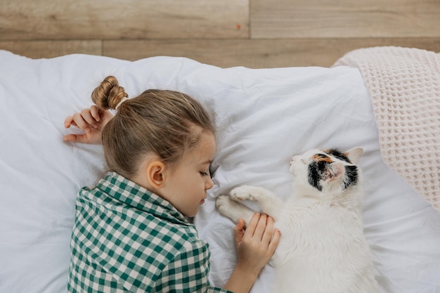 una linda niña de seis años se quedó dormida dulcemente junto a un gato esponjoso en su cama niño con gato dormir en la cama blanca