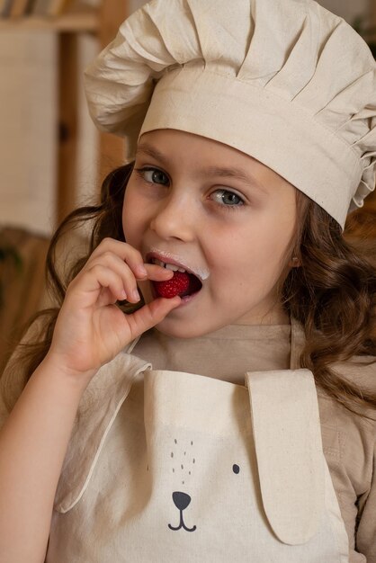 una linda niña de seis años con sombrero de chef come frambuesas