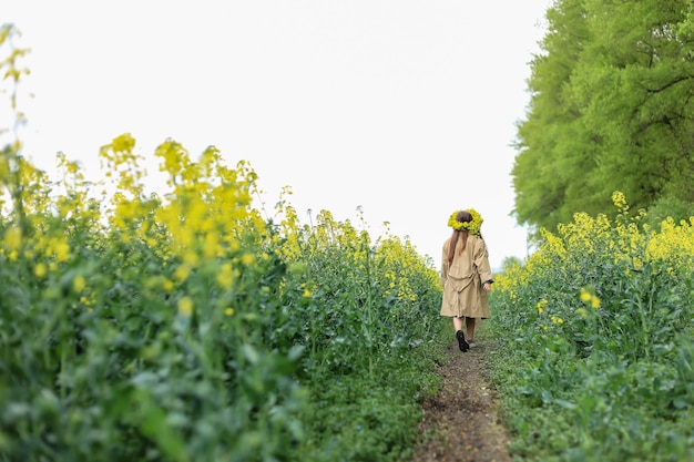 una linda niña de seis años con un vestido de algodón caqui camina por un campo de colza con un ramo