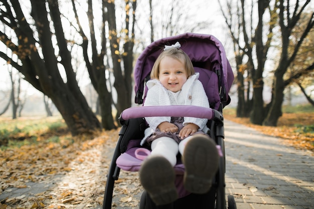 linda niña sentada en el cochecito de bebé púrpura