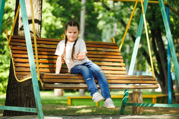 Linda niña sentada en un columpio de madera en un parque verde Vacaciones de verano en el centro turístico del campamento Caminar y jugar al aire libre actividad deportiva y recreación de estilo de vida saludable