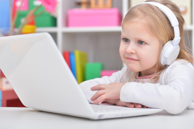 Linda niña sentada en la mesa con la computadora portátil