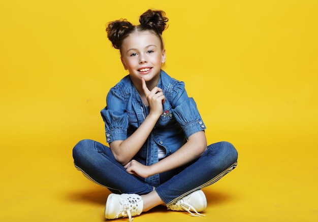 Linda niña sentada y sonriente aislada sobre fondo amarillo