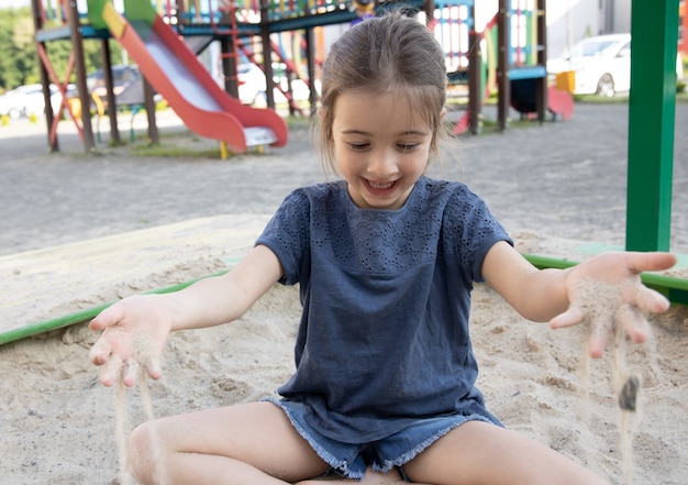 Una linda niña se sienta en un arenero y juega con arena en un caluroso día de verano.