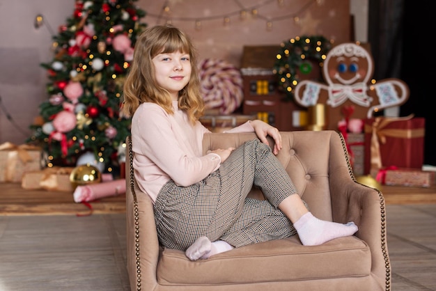 Una linda niña con un sombrero de Papá Noel se sienta en el suelo y mira el marco Año Nuevo