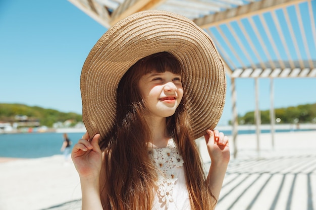 Linda niña con sombrero sonríe en la playa en un día de verano retrato de una niña en la playa