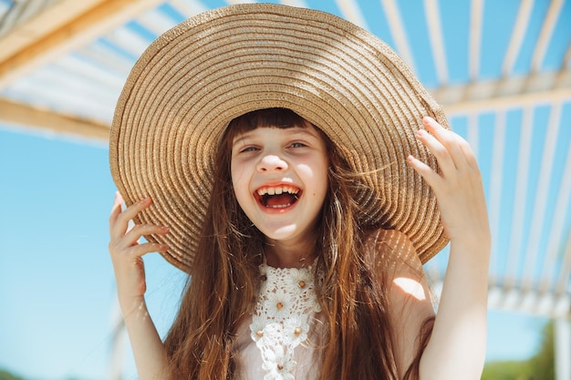 Linda niña con sombrero sonríe en la playa en un día de verano retrato de una niña en la playa