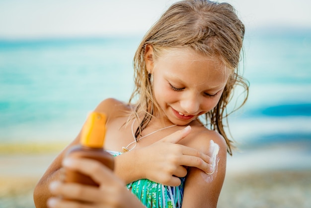 Linda niña sonriente aplicando bronceador en la playa.