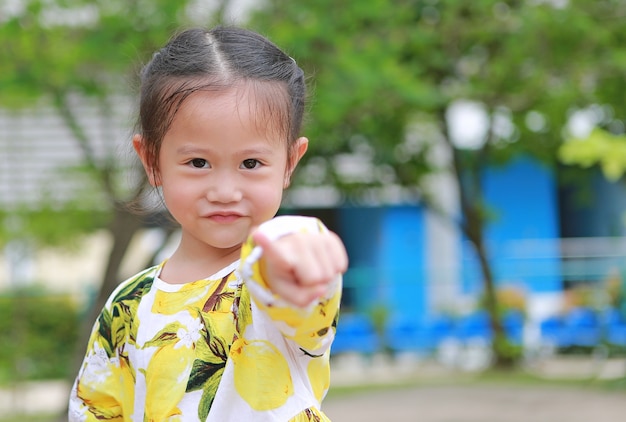 Linda niña sonriente apuntando a la cámara en el jardín.