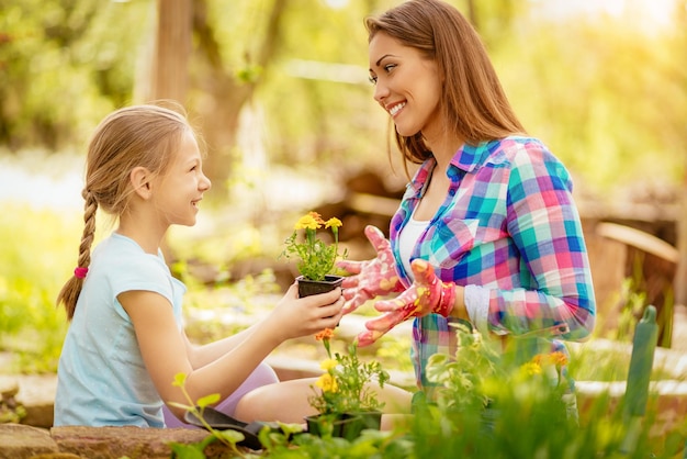 Linda niña sonriente ayudando a su madre a plantar flores en un patio trasero.