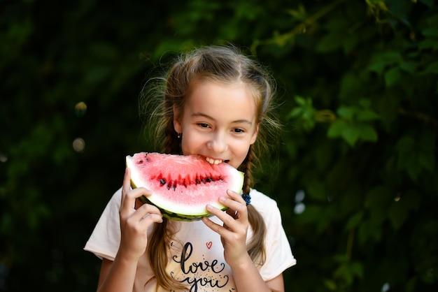 Una linda niña sonriente come una sandía roja Fondo de hojas verdes Naturaleza Comida Verano