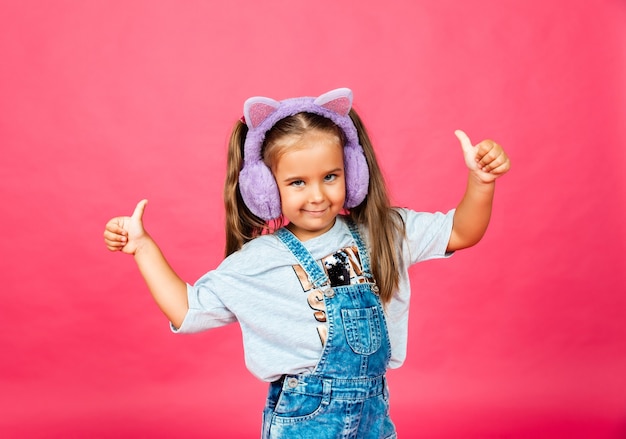 Linda niña sonriente divirtiéndose en auriculares de piel sobre un fondo rosa.