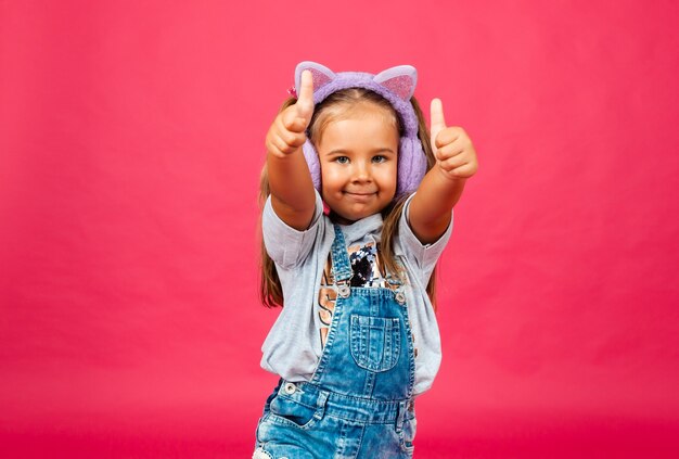 Linda niña sonriente divirtiéndose en auriculares de piel sobre un fondo rosa.