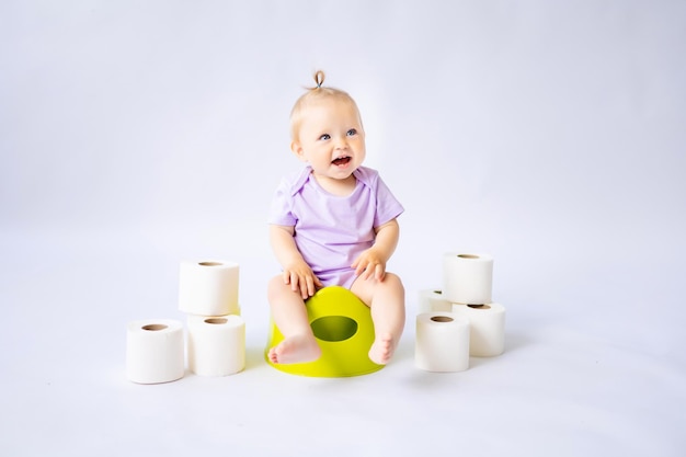 Una linda niña sonriente está sentada en una olla con rollos de papel higiénico aislados en fondo blanco