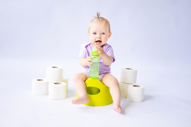 Una linda niña sonriente está sentada en una olla con rollos de papel higiénico aislados en fondo blanco