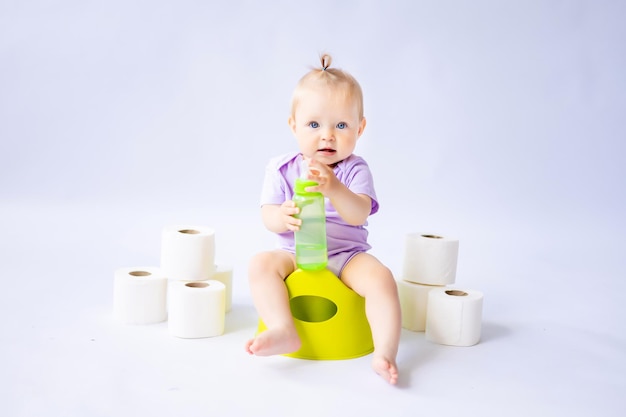 Una linda niña sonriente está sentada en una olla con rollos de papel higiénico aislados en fondo blanco