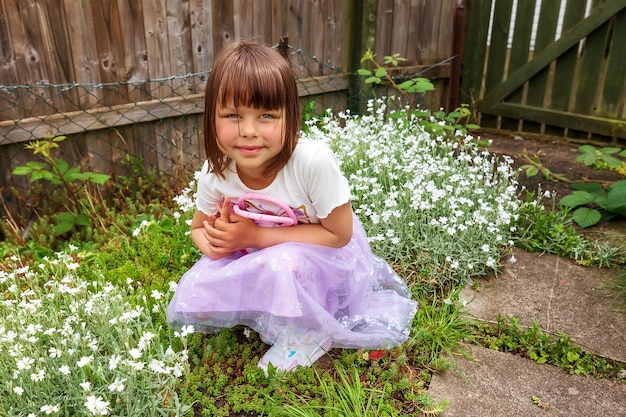 Foto una linda niña sonriente está jugando en el patio trasero con una pequeña bolsa rosa día soleado