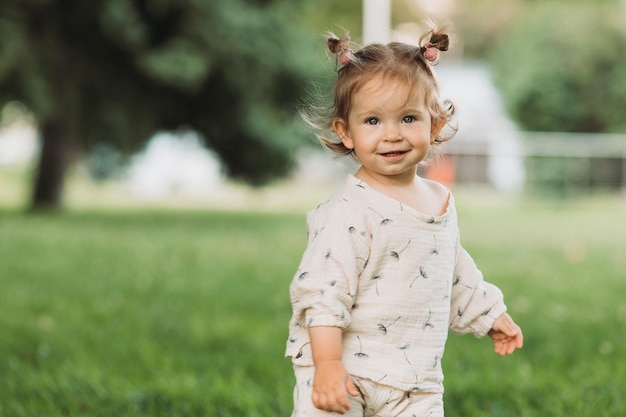 linda niña sonriente con un peinado divertido se esconde detrás de los árboles y corre y juega en el parque